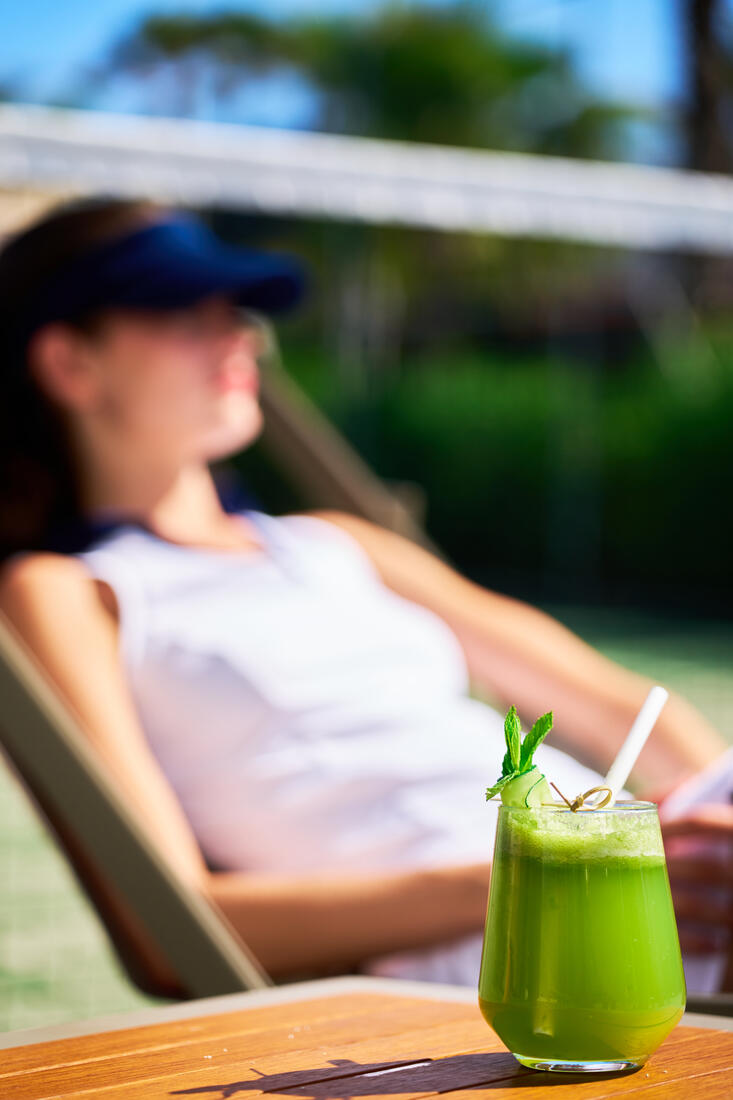 Guest lounging courtside with a green juice at Side Aluna Hotel