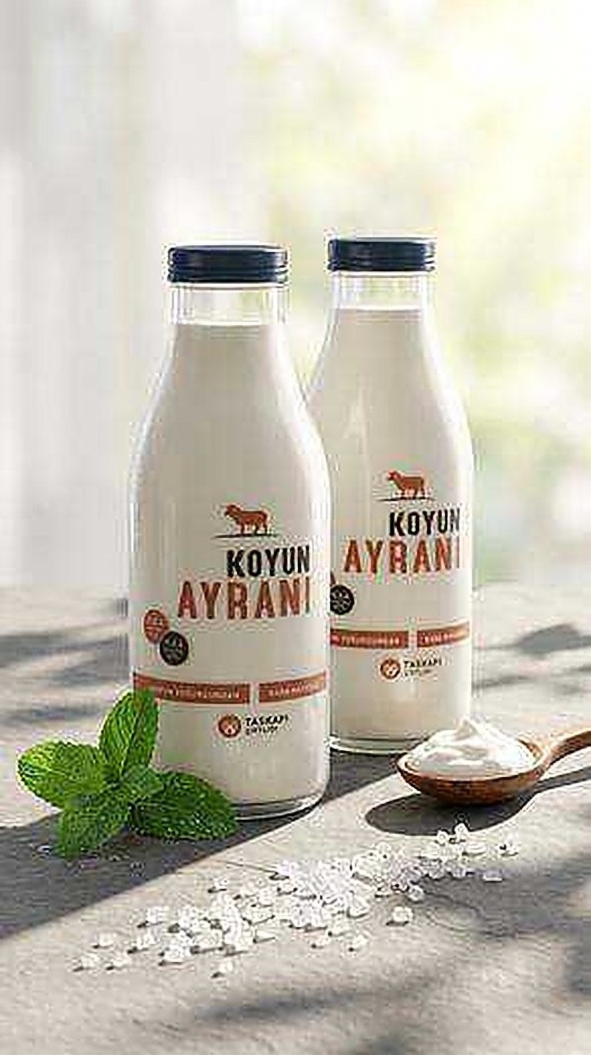 Two Taşkapı Çiftliği ayran bottles with mint leaves and sea salt on a stone surface